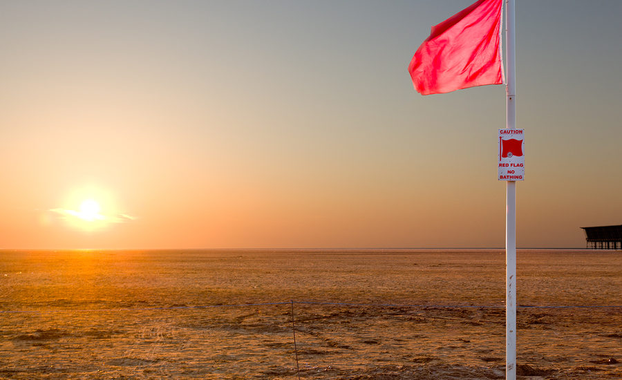 Red flag warning at sunrise on a deserted beach.