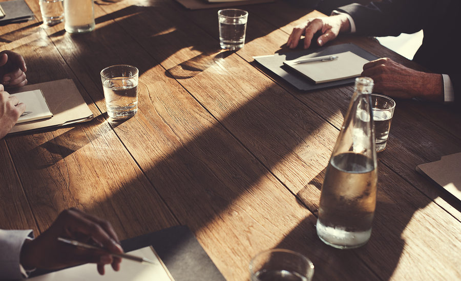 Close-up view of a wooden meeting table with notepads, pens, and glasses of water, creating a professional atmosphere.