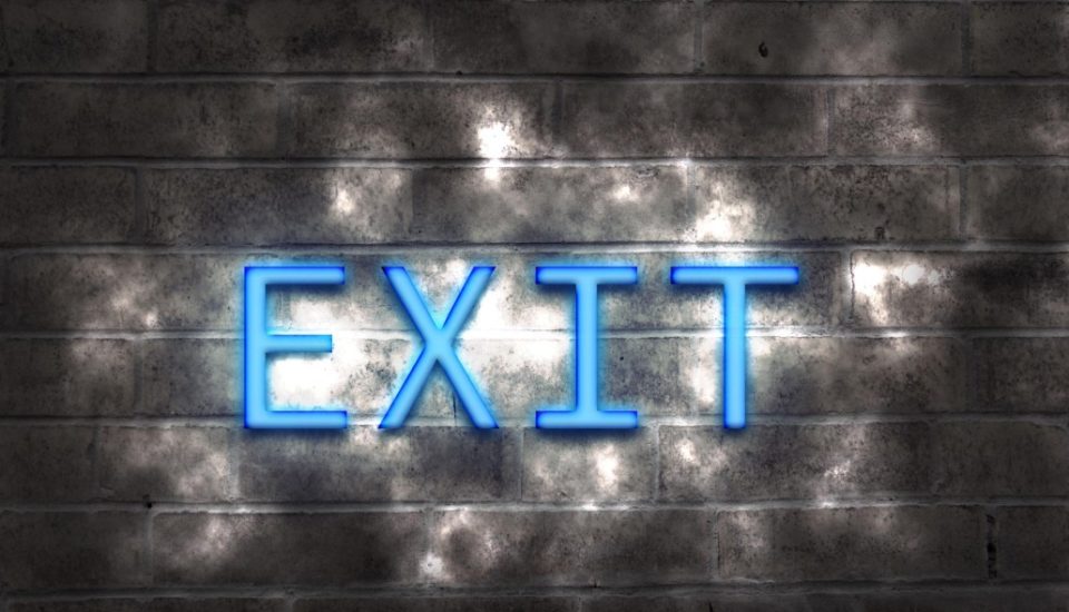 Illuminated blue neon "EXIT" sign on a brick wall with shadows.