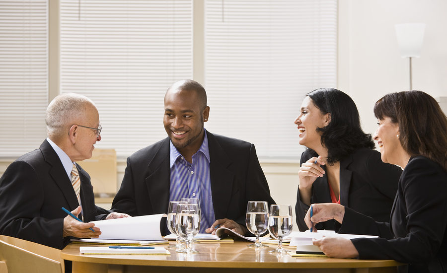 Group of professionals sitting around a table in a meeting, smiling and engaged in discussion.