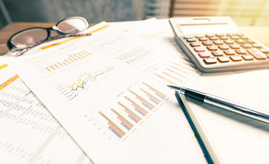 Business financial reports with graphs, calculator, pen, and glasses on a desk.