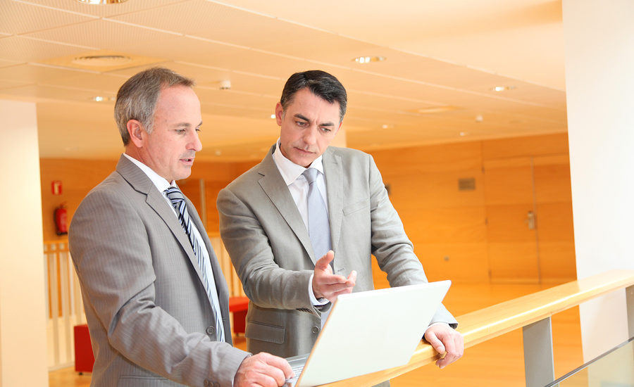 Two business professionals in suits discussing information on a laptop