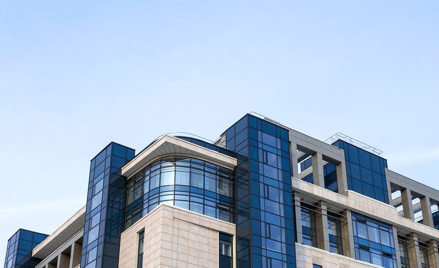 Modern office building with glass and stone facade under a clear blue sky.