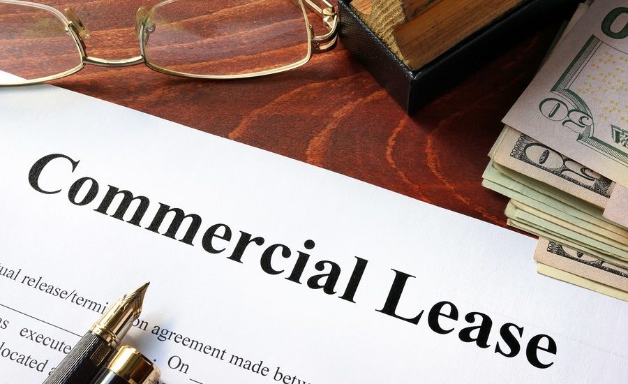 A commercial lease document on a wooden desk with a pair of reading glasses, a pen, and a book in the background.