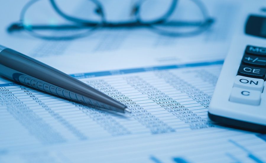 A close-up image of a financial spreadsheet with numerical data, a pen resting on the document, and a pair of eyeglasses in the background, partially out of focus.