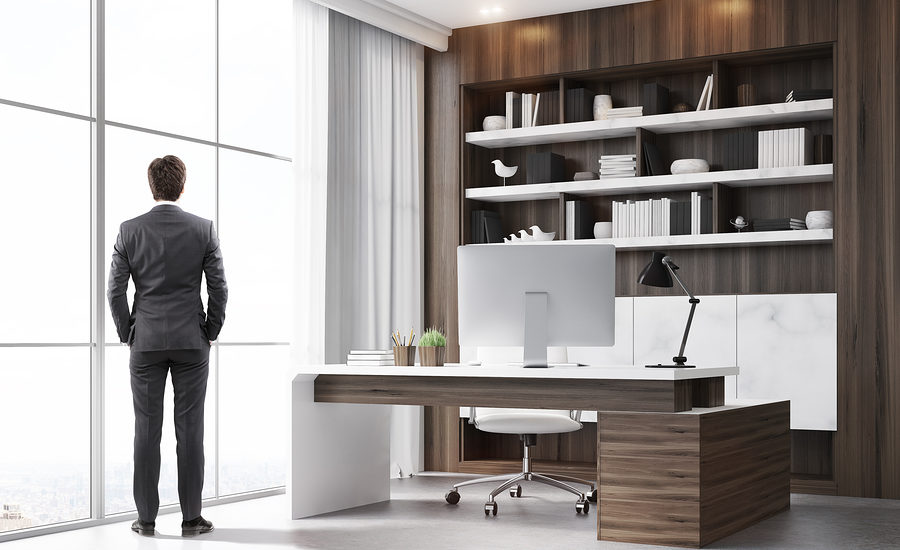 Professional man in a suit standing in a modern office with floor-to-ceiling windows, looking out over the city skyline.
