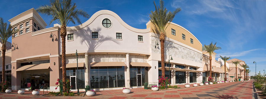 Exterior view of a retail plaza with palm trees and a clear blue sky.
