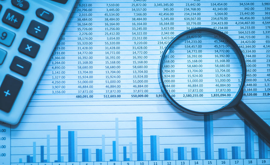 Financial data and analysis with a magnifying glass and calculator on a table.
