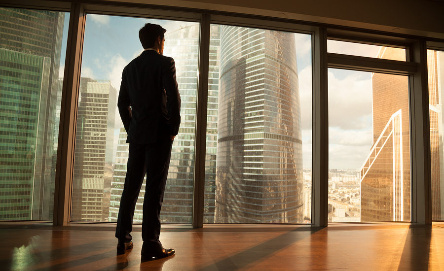 Business professional standing in front of large windows overlooking a city skyline.