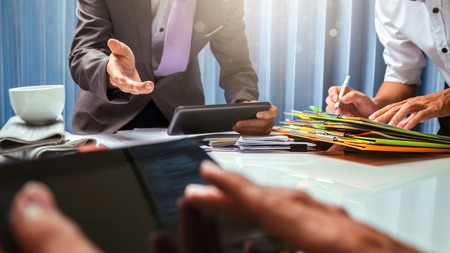 Business professionals discussing documents and using tablets during a meeting.