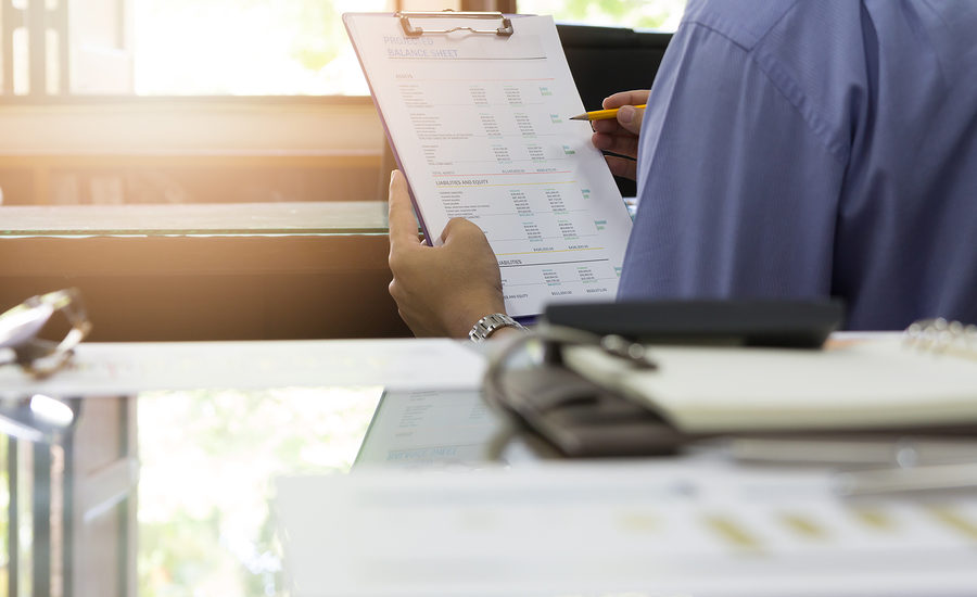 Business professional reviewing a balance sheet on a clipboard with a pen in hand