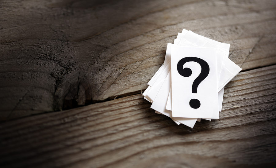 A stack of small white cards with a bold black question mark on top, placed on a rustic wooden surface.