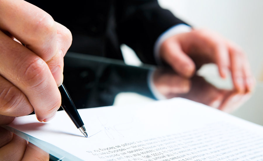 Businessperson signing a document on a glass desk.