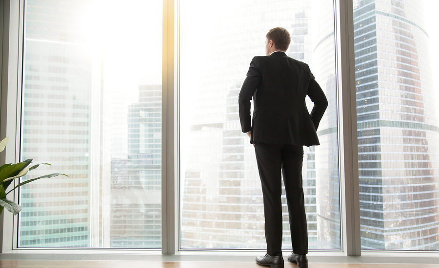 Business professional standing by a large window overlooking a cityscape.