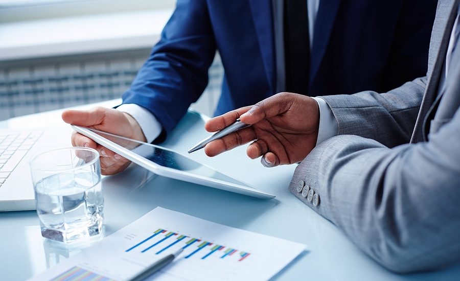 Close-up of two business professionals discussing data on a tablet and reviewing documents with graphs.