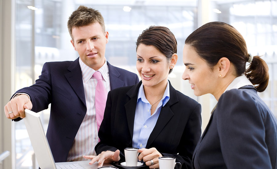 A group of business professionals in a meeting, discussing ideas and reviewing information on a laptop.