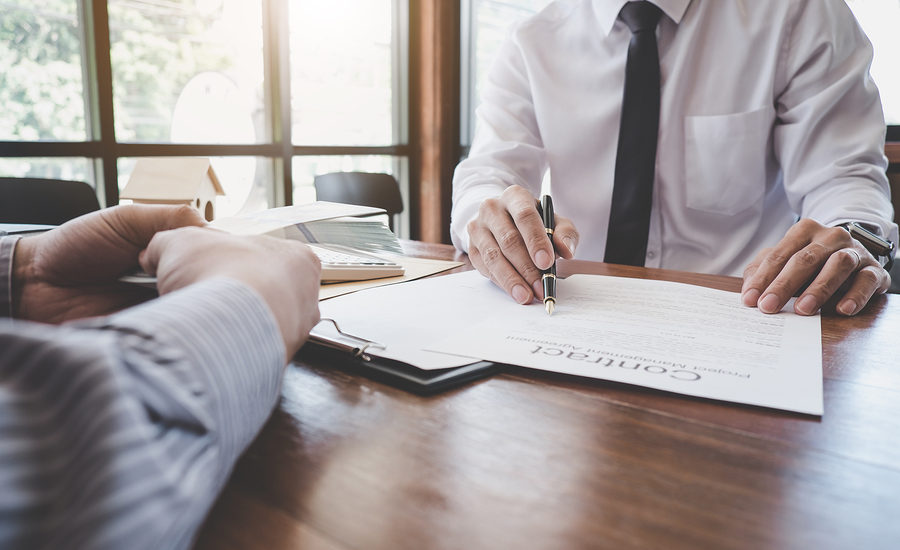 Businessperson signing a contract with a client at a wooden desk.