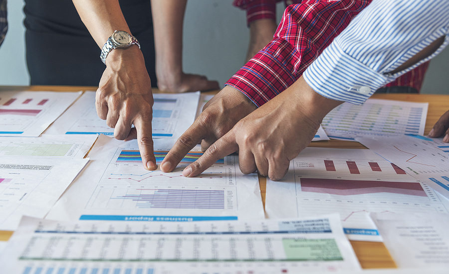 Hands of business professionals pointing at charts and graphs on a table, emphasizing collaboration and analysis.