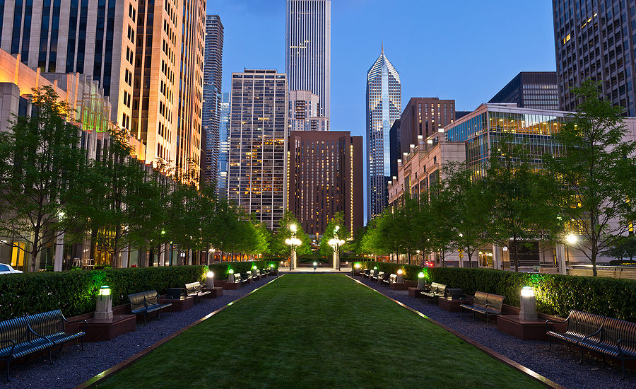 Beautiful urban park with lush green lawns and benches surrounded by skyscrapers at twilight.