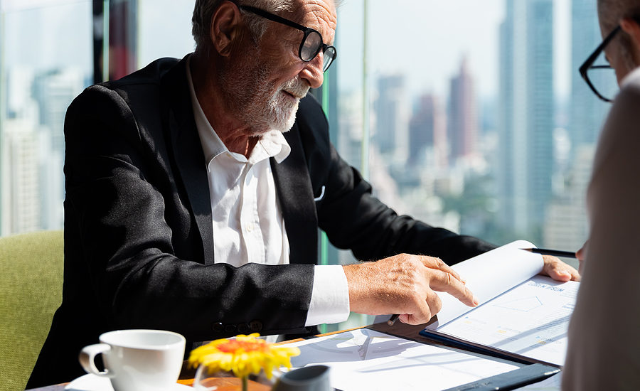 Mature businessman analyzing a document in a high-rise office with a cityscape in the background.