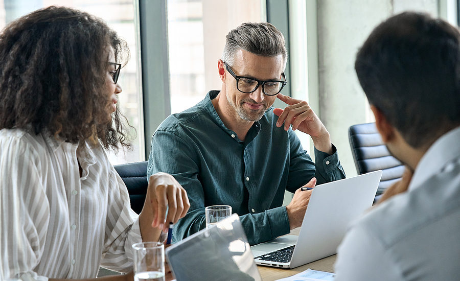 Diverse business team in a meeting, discussing ideas while working on a laptop.