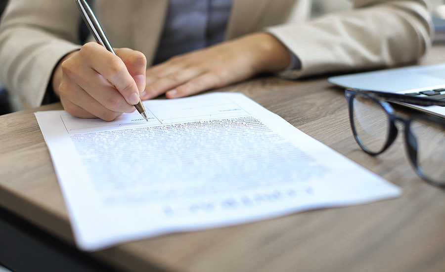 Close-up of a business professional signing a document at a wooden desk.