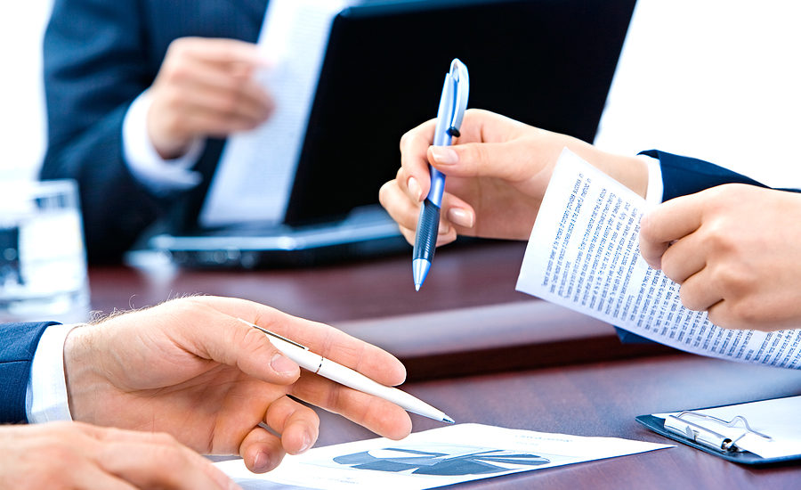 Close-up of business professionals exchanging documents and pens during a meeting.