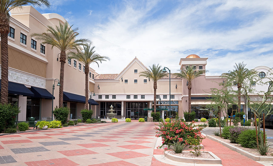 Modern outdoor shopping plaza with palm trees and a fountain.