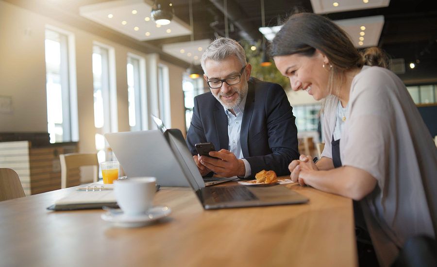 Two business professionals smiling and collaborating on laptops during a meeting.