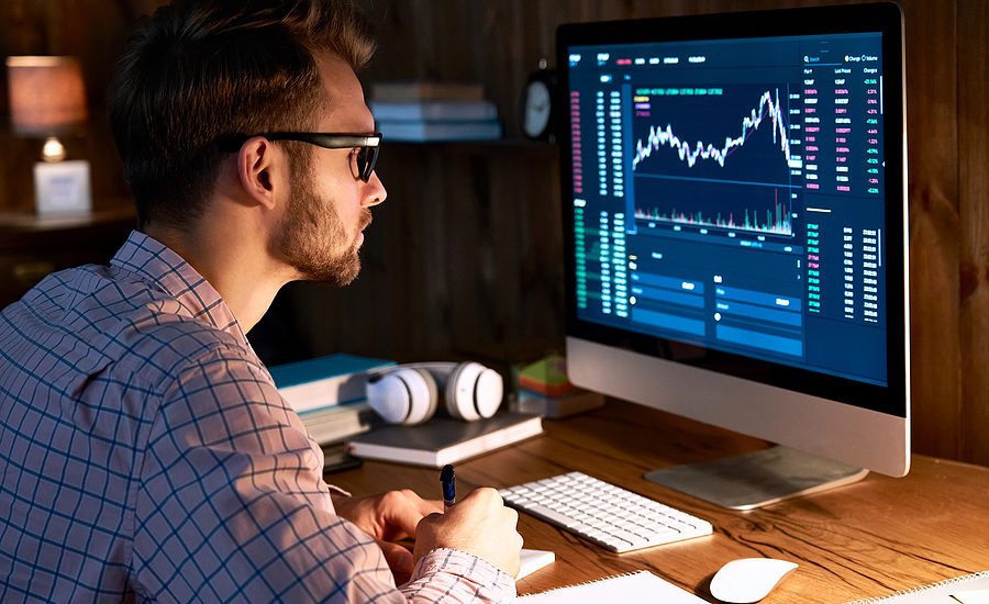 Focused trader analyzing stock market data on a computer screen in a home office.