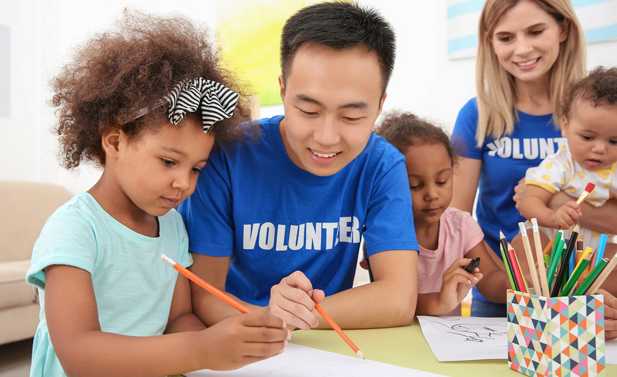 A volunteer assisting children with drawing activities at a community event.
