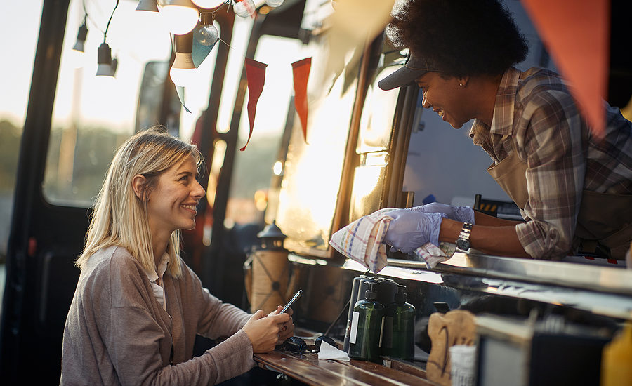 Friendly interaction between a smiling food truck vendor and a happy customer.
