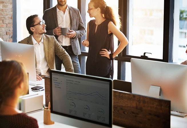 Team discussing business strategies in a modern office with computers displaying data charts.