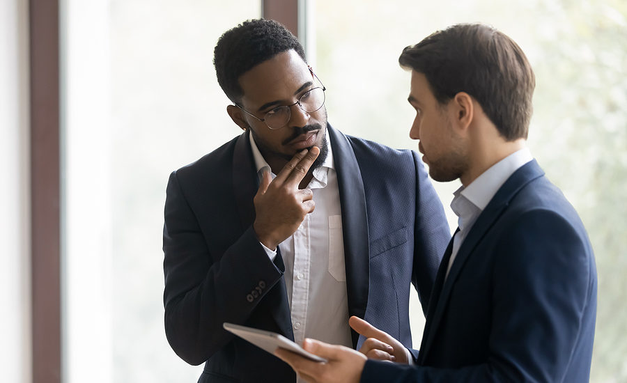 Two business professionals engaged in a thoughtful discussion, with one holding a tablet, symbolizing decision-making and collaboration.