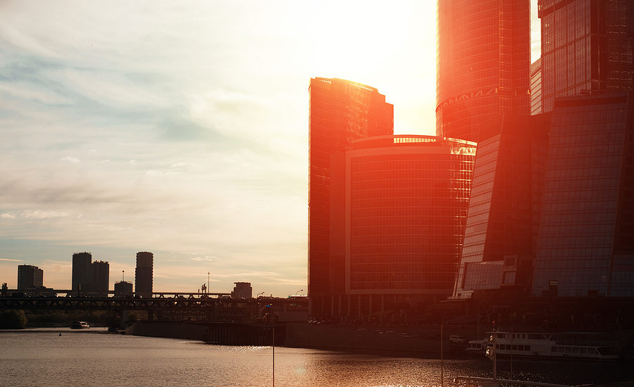 Modern city skyline at sunset with towering office buildings reflecting sunlight over the water.