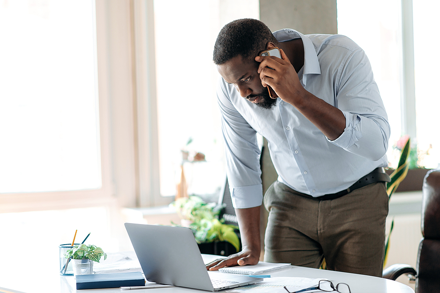 Focused businessman speaking on the phone while working on a laptop at his office desk.