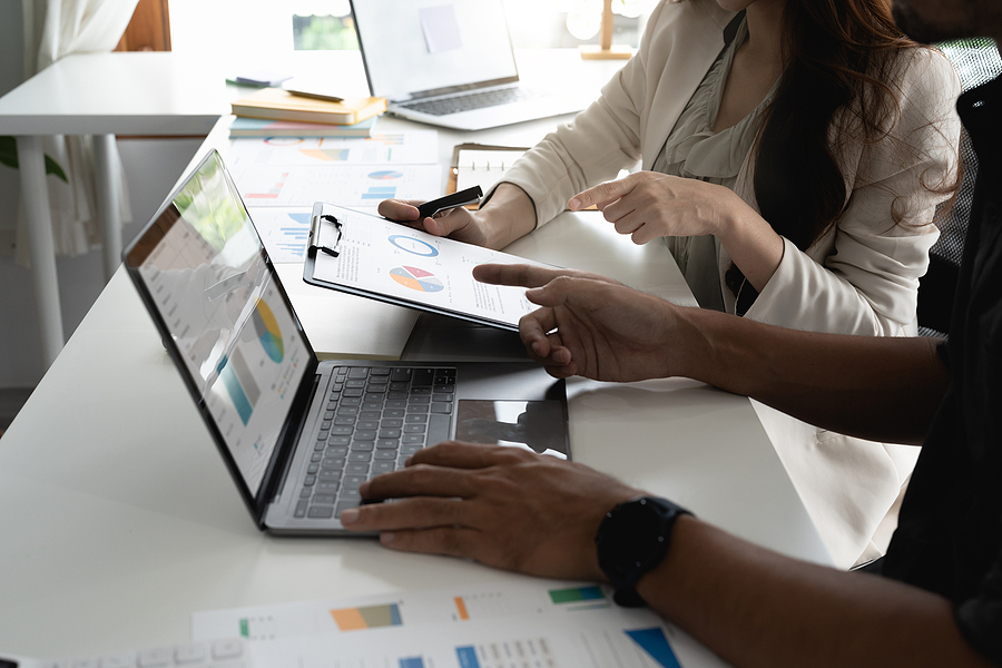 Business professionals reviewing financial reports with graphs and charts on a laptop and clipboard.