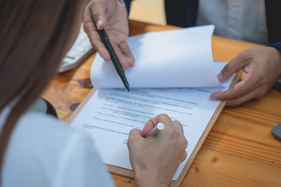Close-up of individuals reviewing and signing a contract document on a wooden desk.