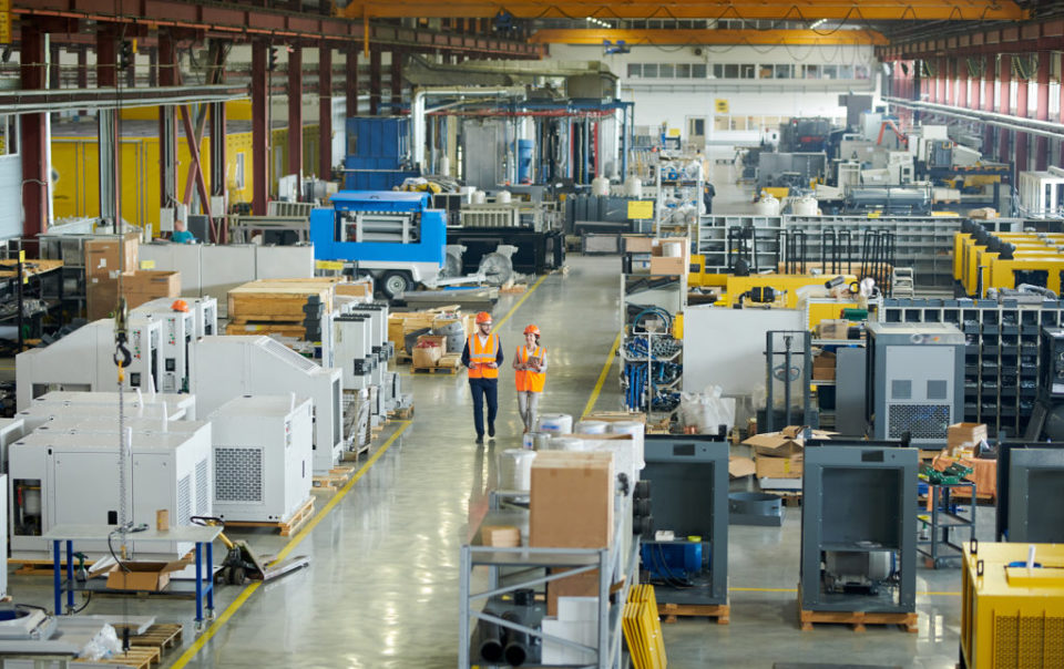 Workers in safety vests walking through a large industrial manufacturing facility.