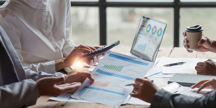 Business team analyzing financial reports with a calculator and charts displayed on a laptop.