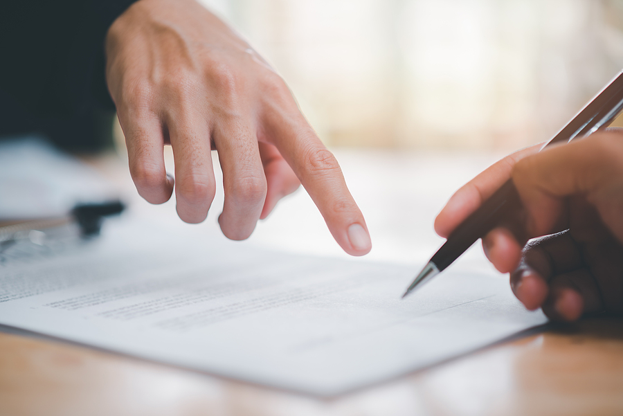 Hand pointing at a document with another hand holding a pen.