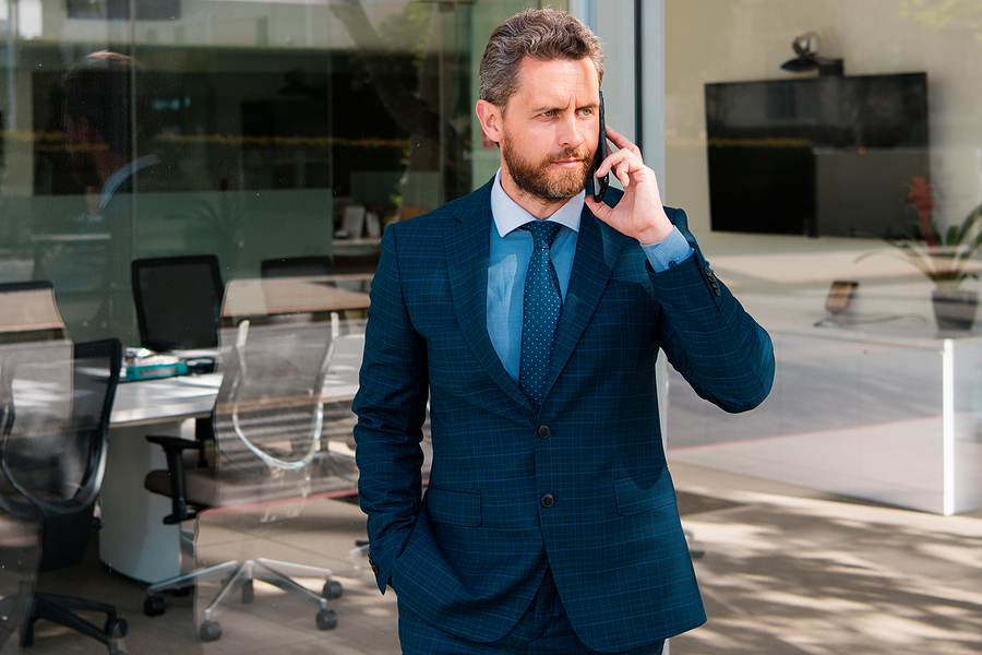 Businessman in a blue suit talking on the phone outside a modern office building.