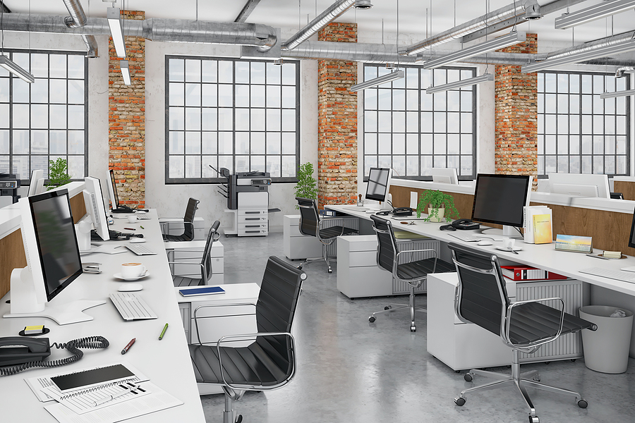 Modern open-plan office with desks, computers, and exposed brick walls.