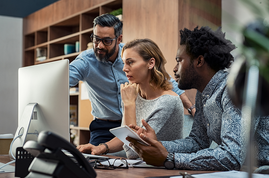 Three business professionals collaborating around a computer in a modern office setting.