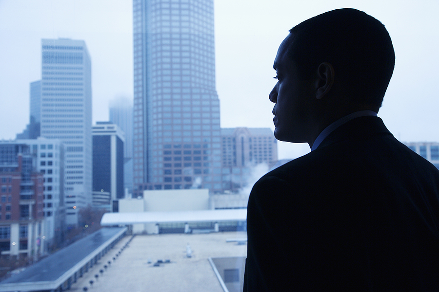 Businessman standing by a window, looking out at a city skyline in a contemplative pose.