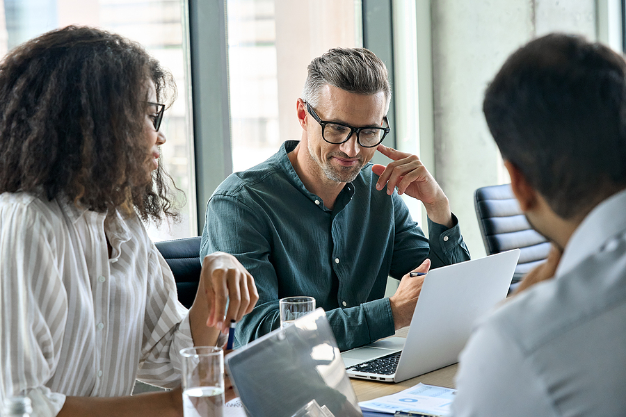 Diverse business team in a meeting, discussing ideas while working on a laptop.