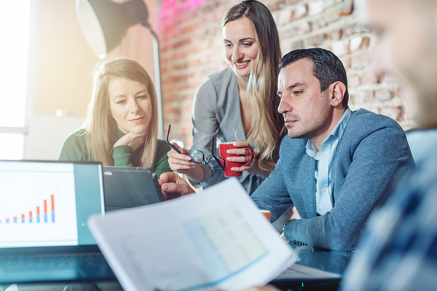 Group of colleagues collaborating around a table with a tablet and documents in a casual office setting.