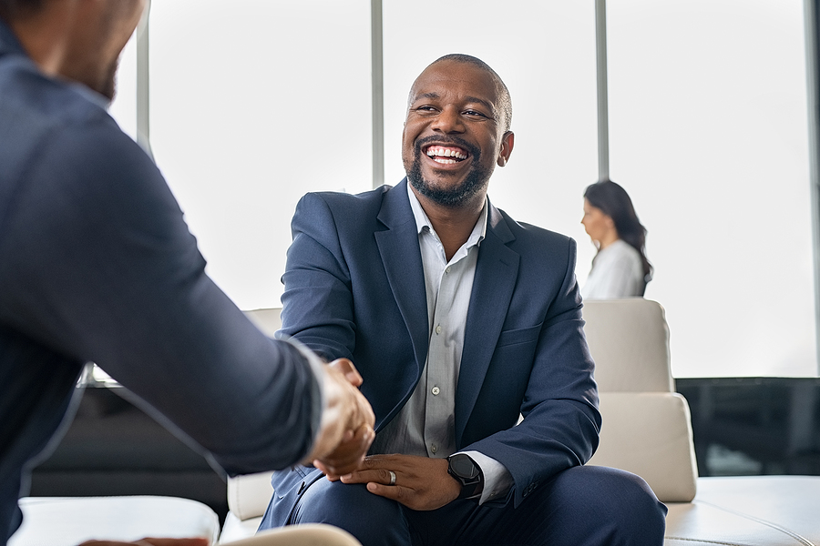 Smiling businessman in a suit shaking hands during a meeting in a modern office setting.