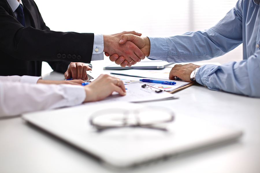 Professional handshake during a business meeting with documents and pens on the table.