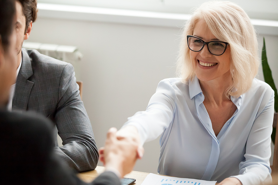 Smiling professional woman in glasses shaking hands during a business meeting.